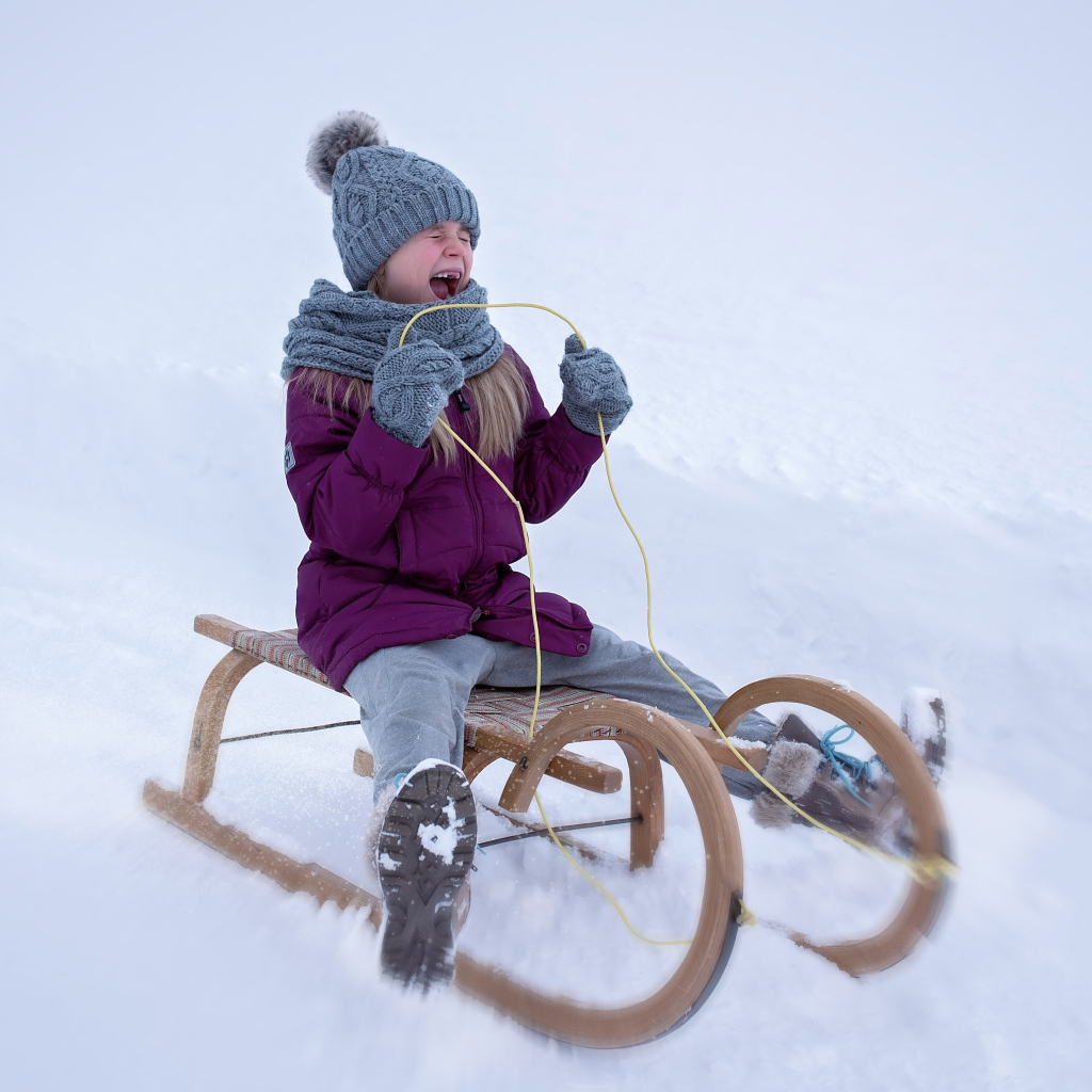 Маленькая девочка едет на санях с горки зимой