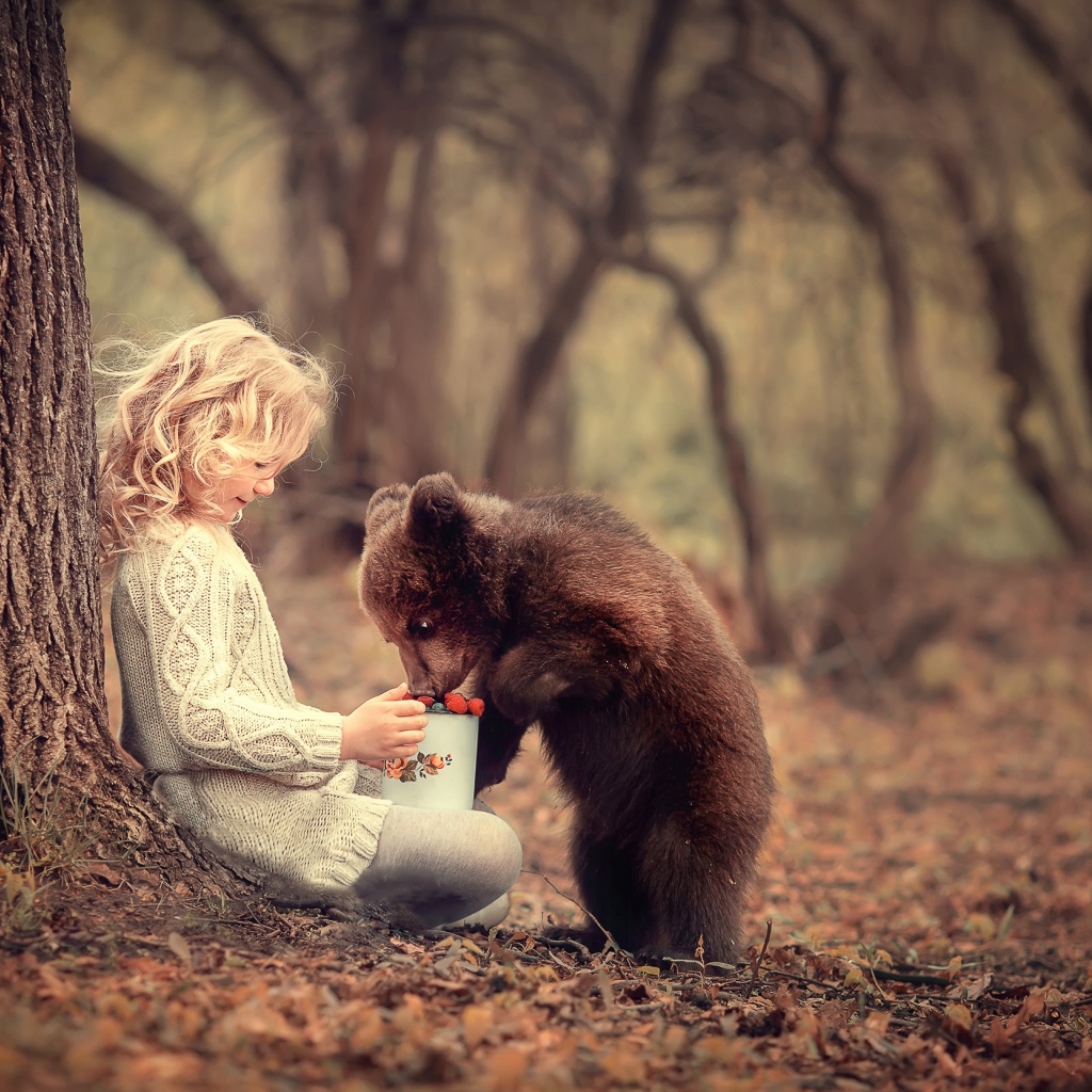 Маленькая девочка сидит у дерева с медвежонком гризли