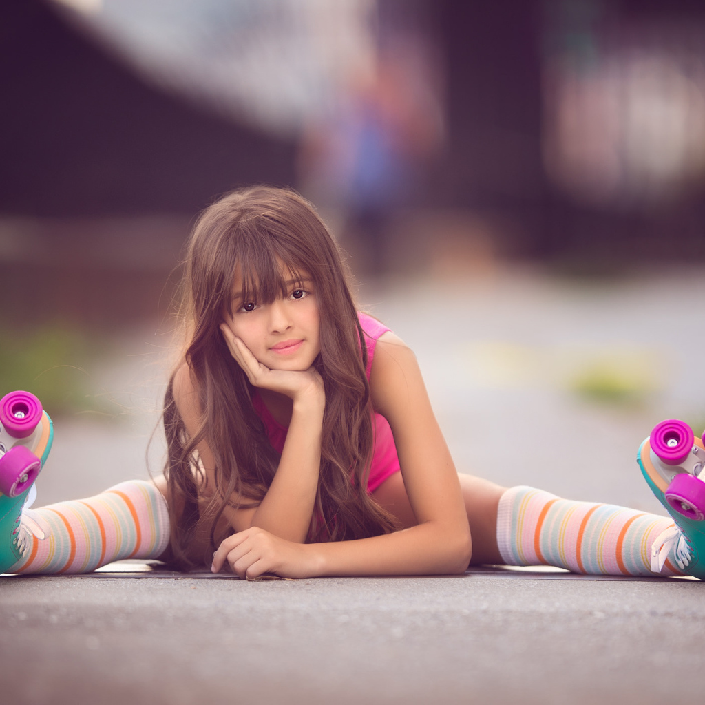 Маленькая девочка сидит на дороге в роликах