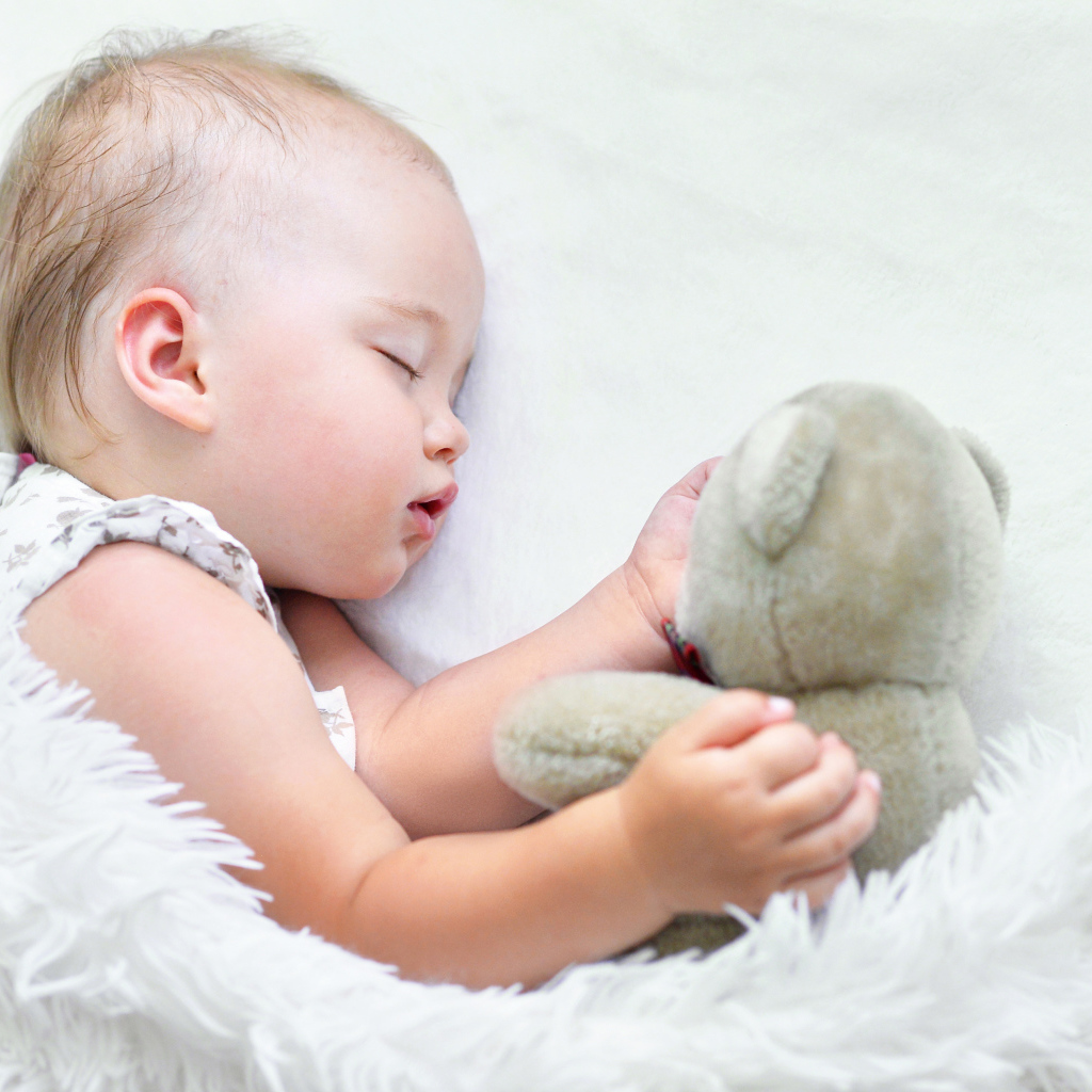 Маленькая девочка спит с мягкой игрушкой под белым одеялом