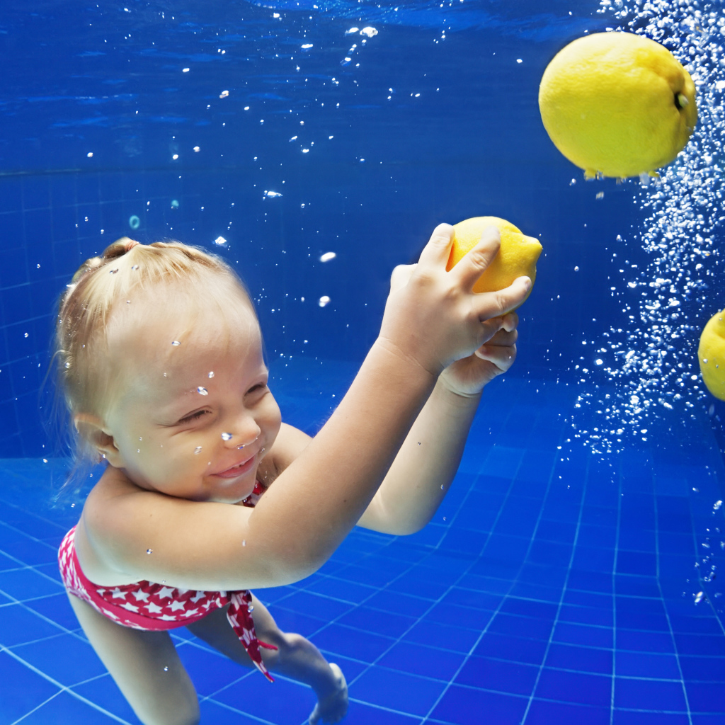 Маленькая девочка плавает в бассейне с желтыми лимонами