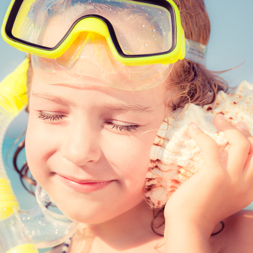 Маленькая девочка приложила ракушку к уху