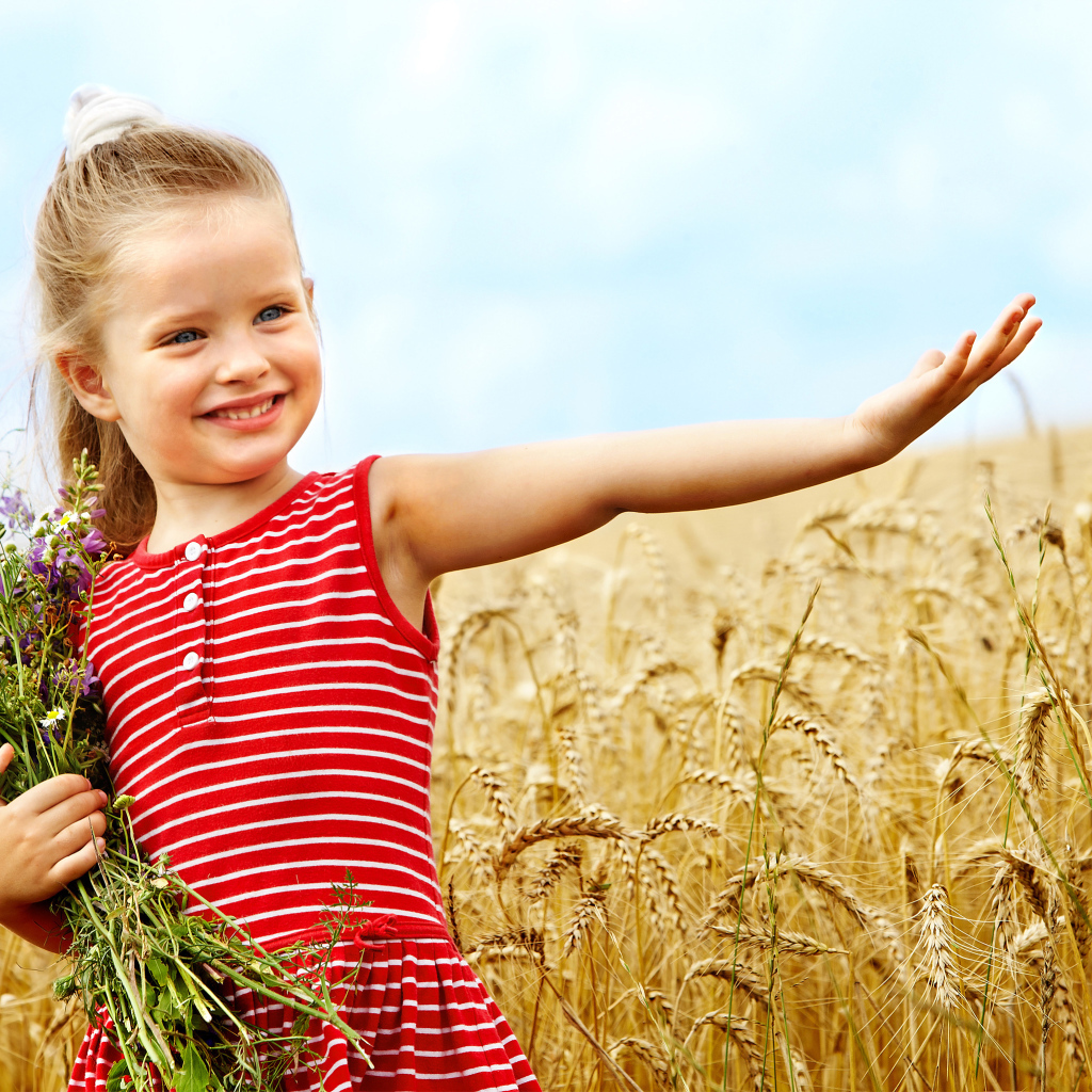 Маленькая девочка с букетом полевых цветов гуляет по полю пшеницы