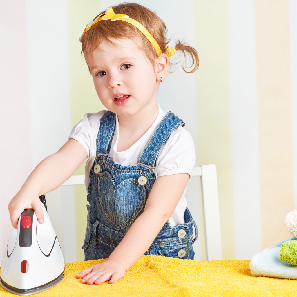 Маленькая девочка с утюгом гладит полотенце