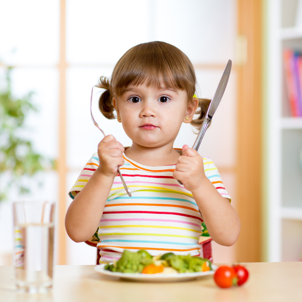 Маленькая девочка со столовыми приборами и тарелкой