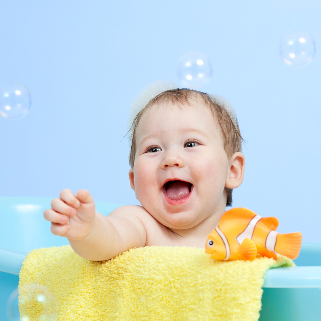 Веселый малыш купается в ванной с игрушечной рыбкой