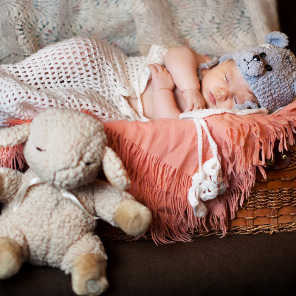 Спящий грудной ребенок в забавной шапке с мягкой игрушкой