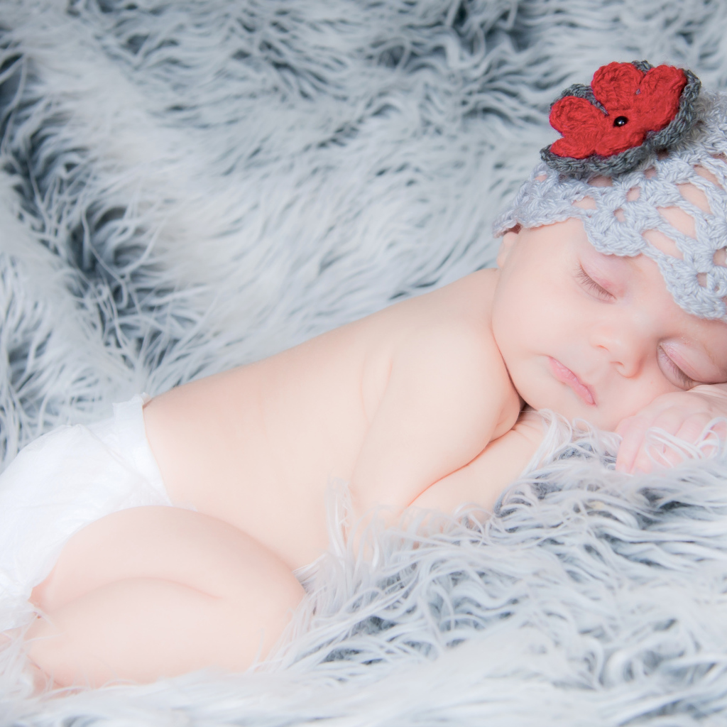 Спящий грудной ребенок в вязаной шапке с красным цветком на голове