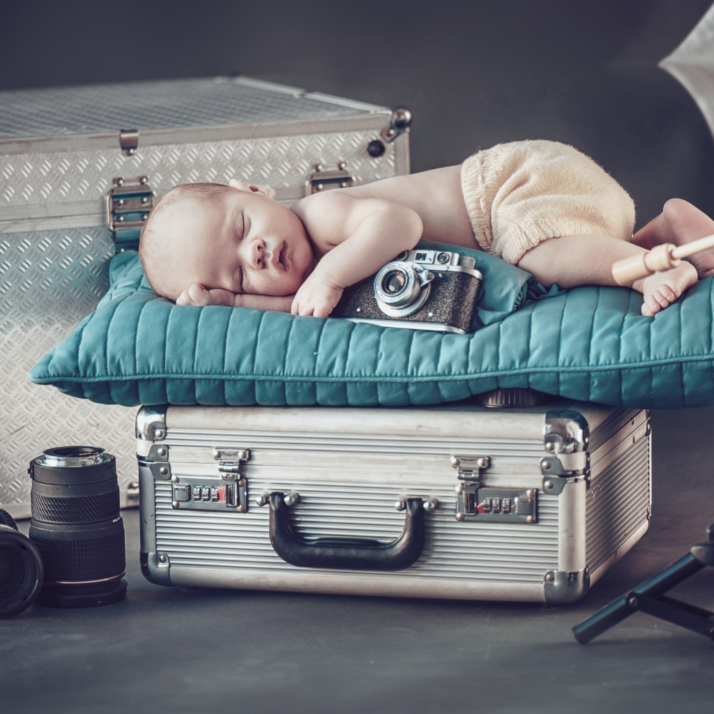 Спящий младенец с фотоаппаратом спит на чемодане