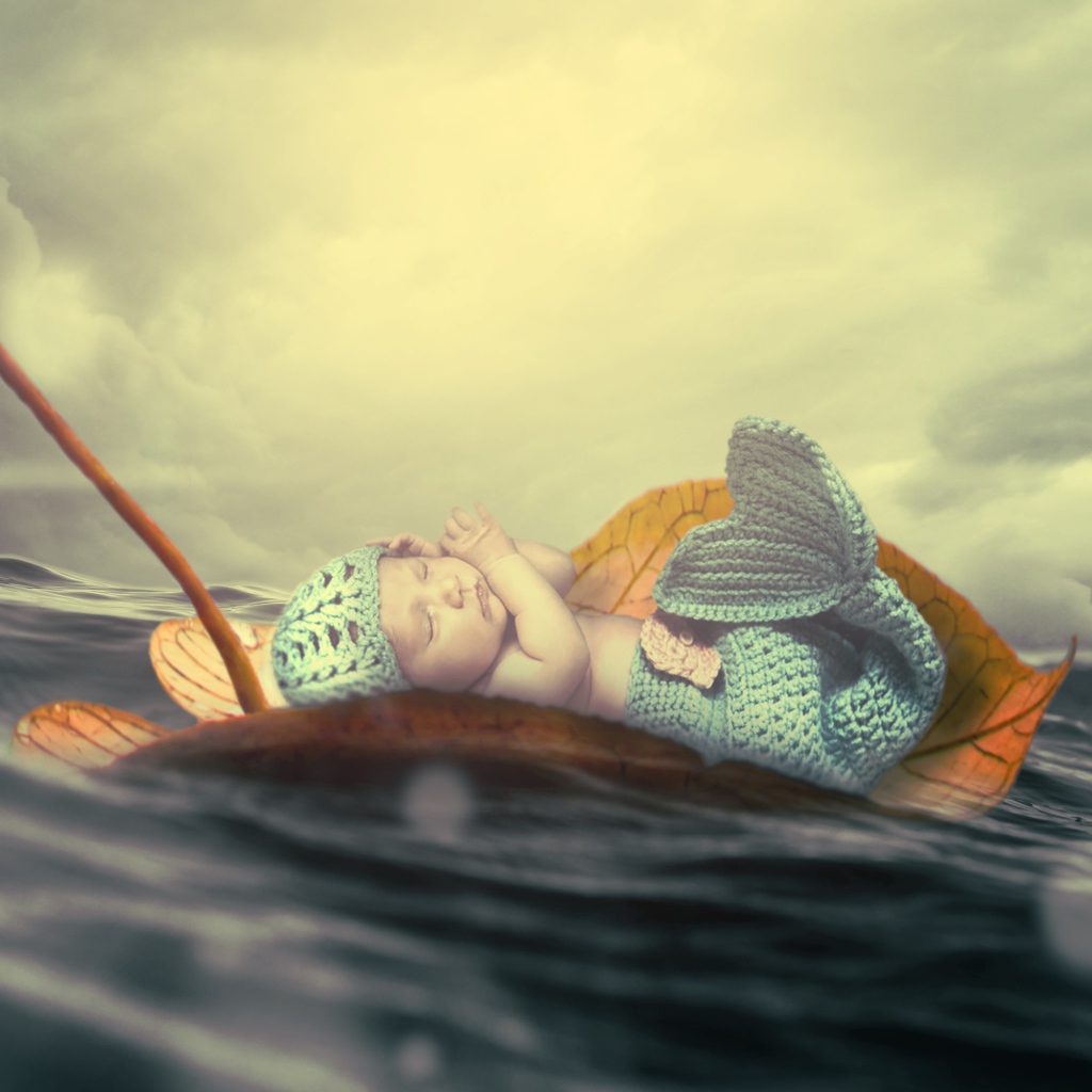 Маленький грудной ребенок в костюме русалки плывет на листе в океане
