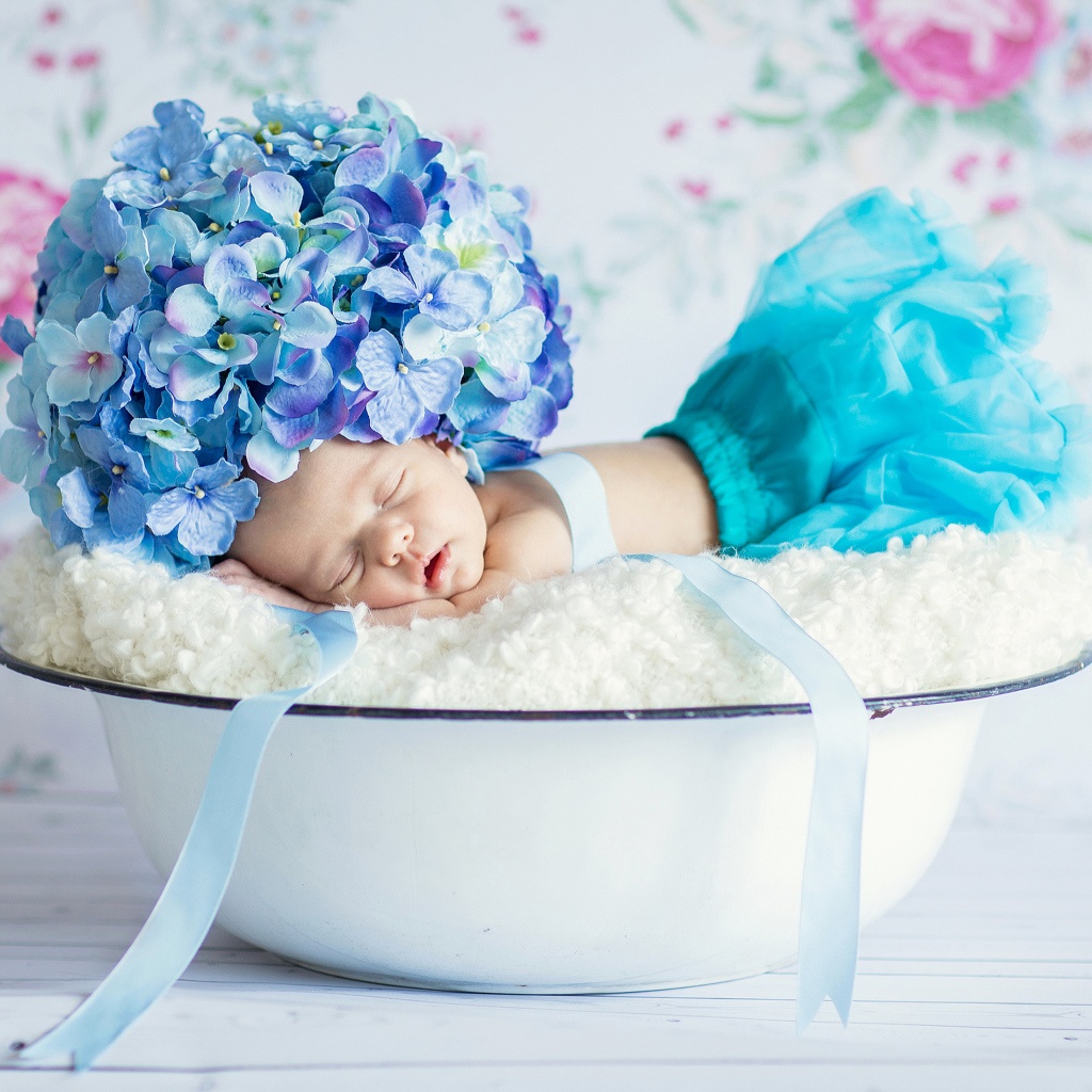 Маленький грудной ребенок спит в миске с шапкой из цветов гортензии на голове