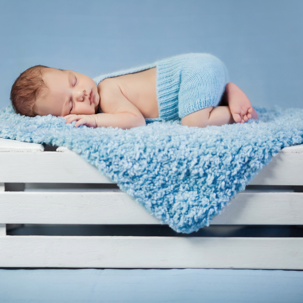 Маленький грудной ребенок спит на синем покрывале на деревянном ящике