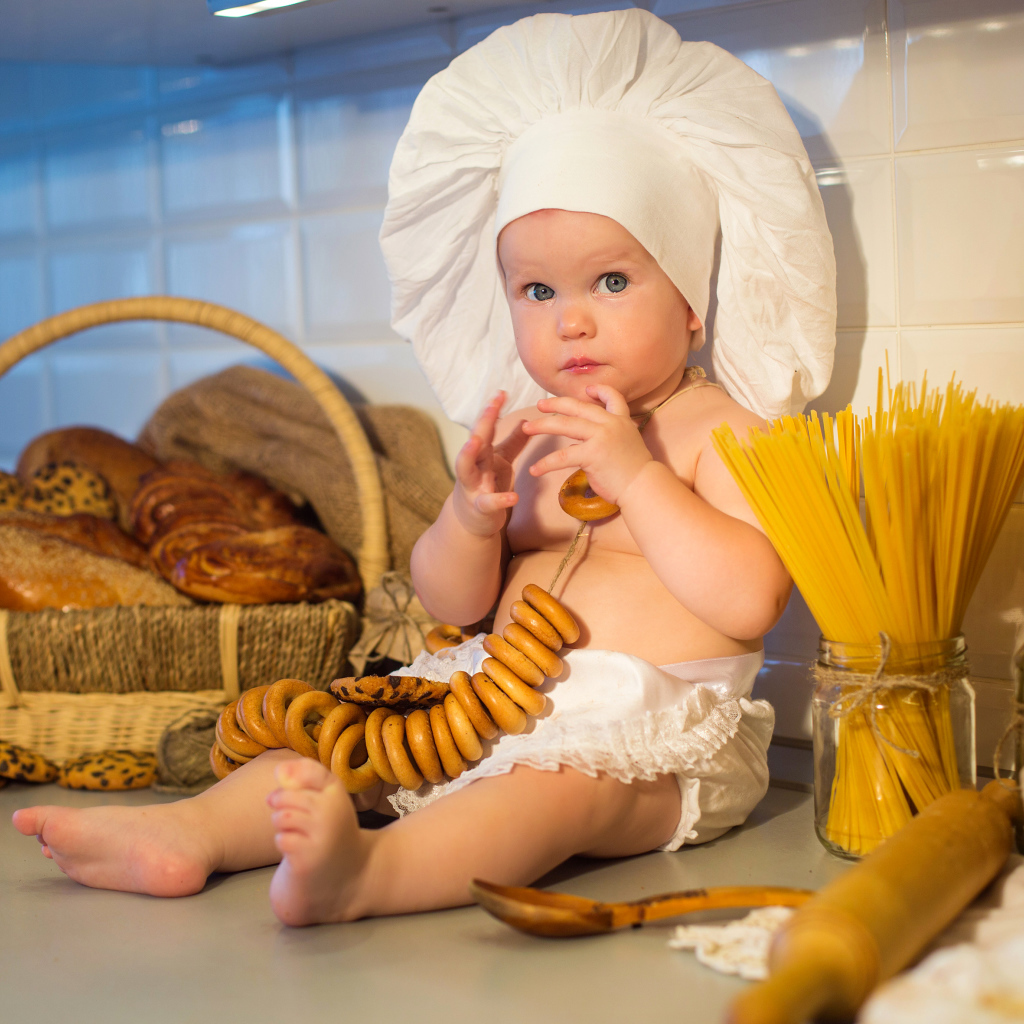 Маленький ребенок в шапке повара сидит на столе с выпечкой