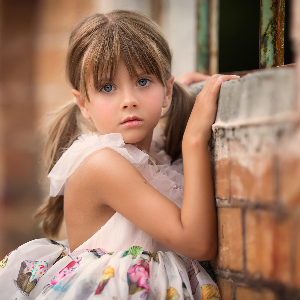 Милая девочка с серьезным взглядом стоит у стены