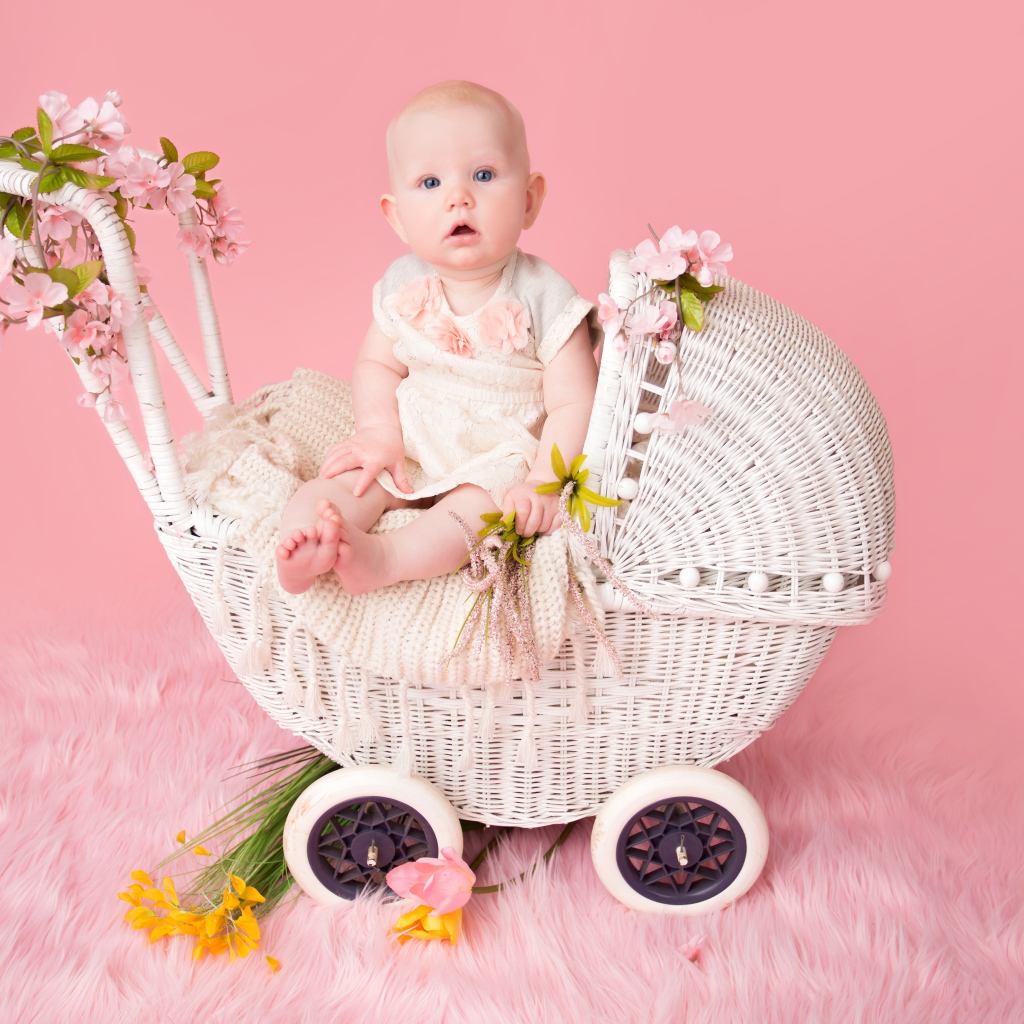 Младенец девочка сидит в коляске на розовом фоне