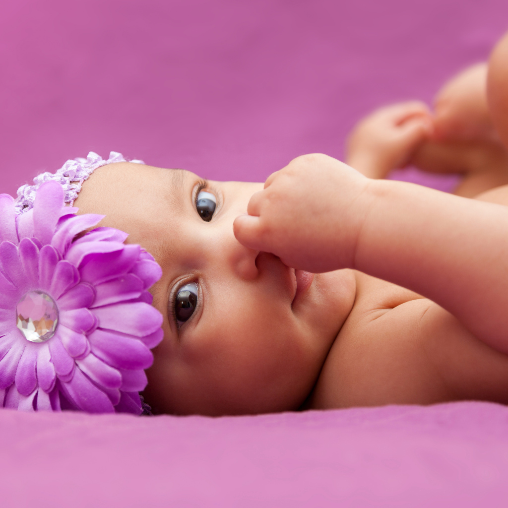 Младенец девочка с большим сиреневым цветком на голове 
