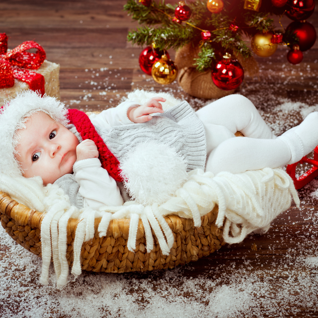 Младенец в корзине в новогоднем костюме под елкой с подарками