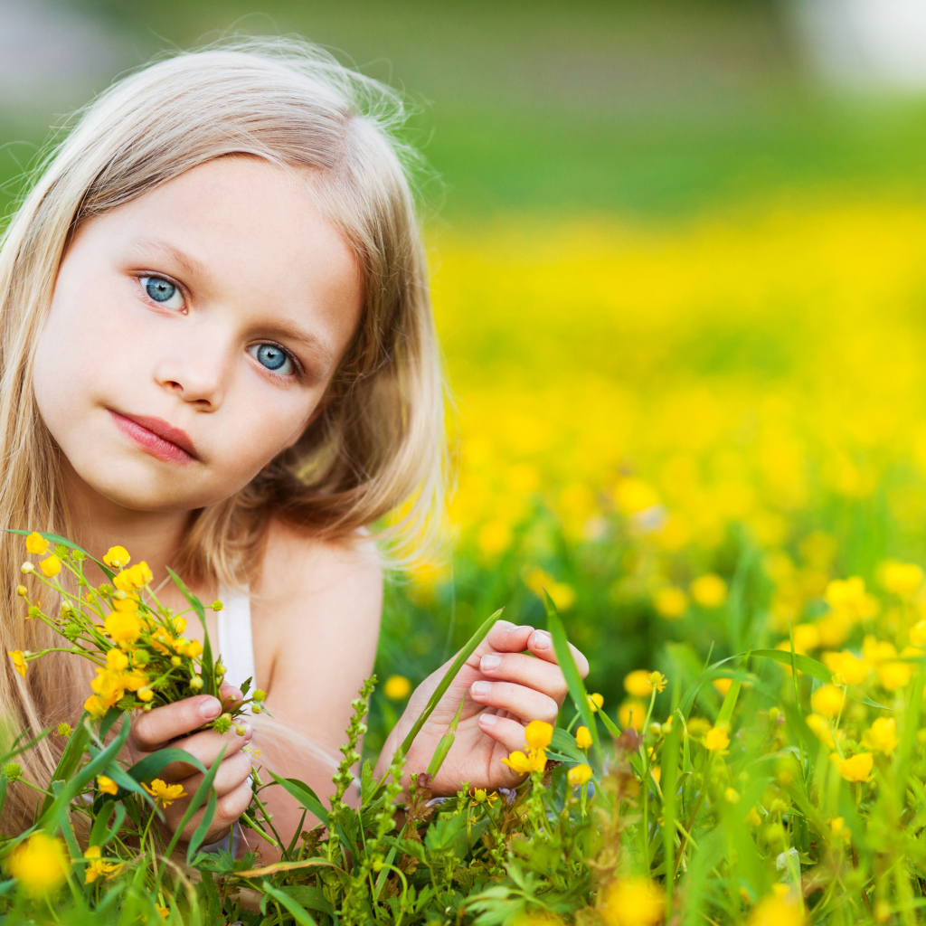 Красивая голубоглазая девочка лежит на желтых полевых цветах