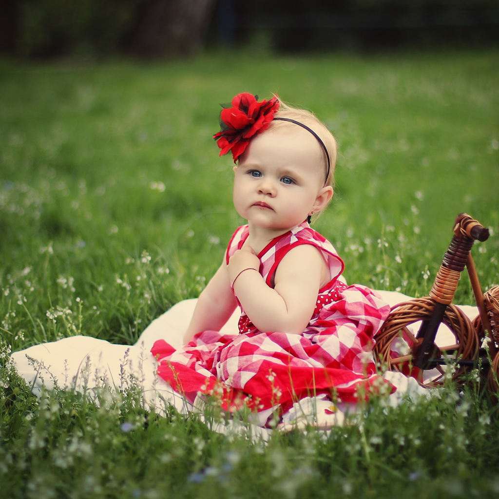 Красивая маленькая девочка с красным цветком на голове сидит на зеленой траве