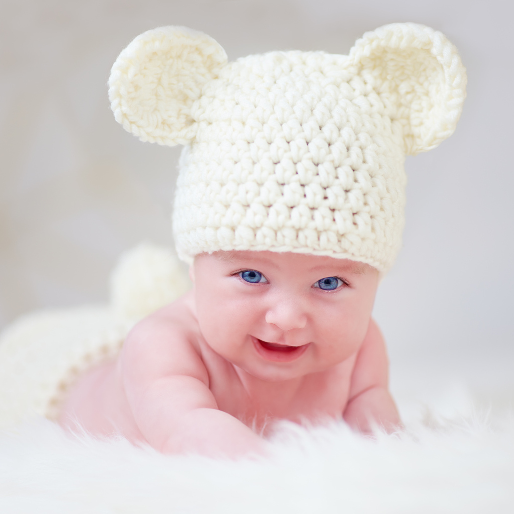 Голубоглазый грудной ребенок в белой вязаной шапке с ушками