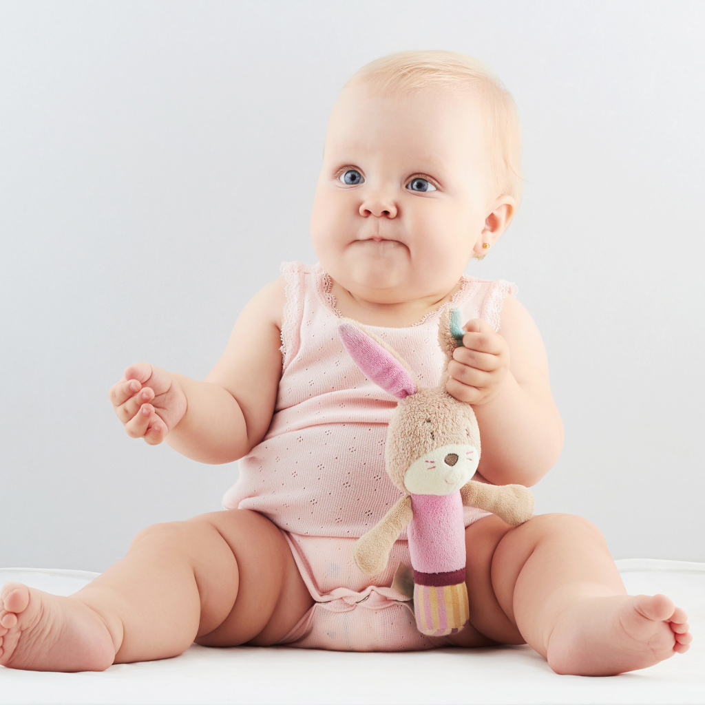 Голубоглазый младенец с мягкой игрушкой на сером фоне
