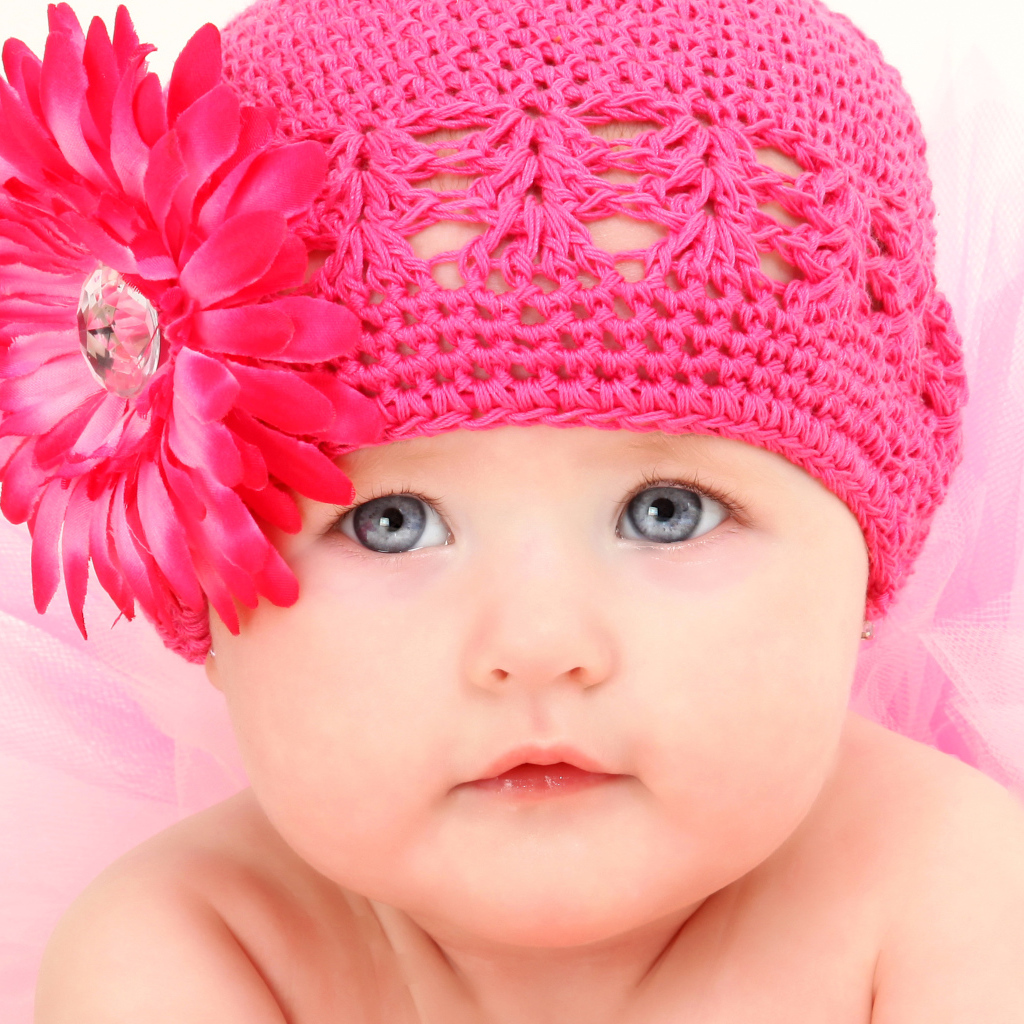 Милая голубоглазая малышка в розовой шапке с цветком герберы