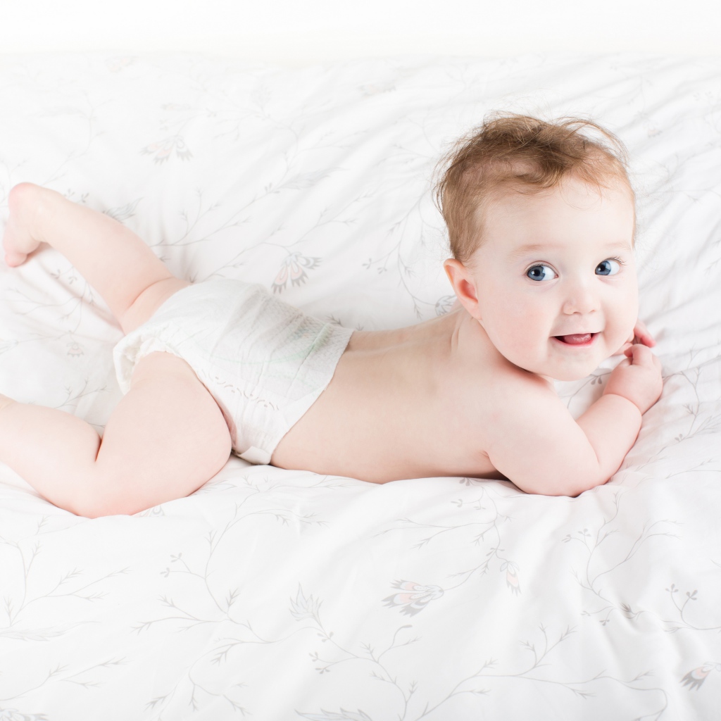 Забавный голубоглазый малыш лежит на белом покрывале