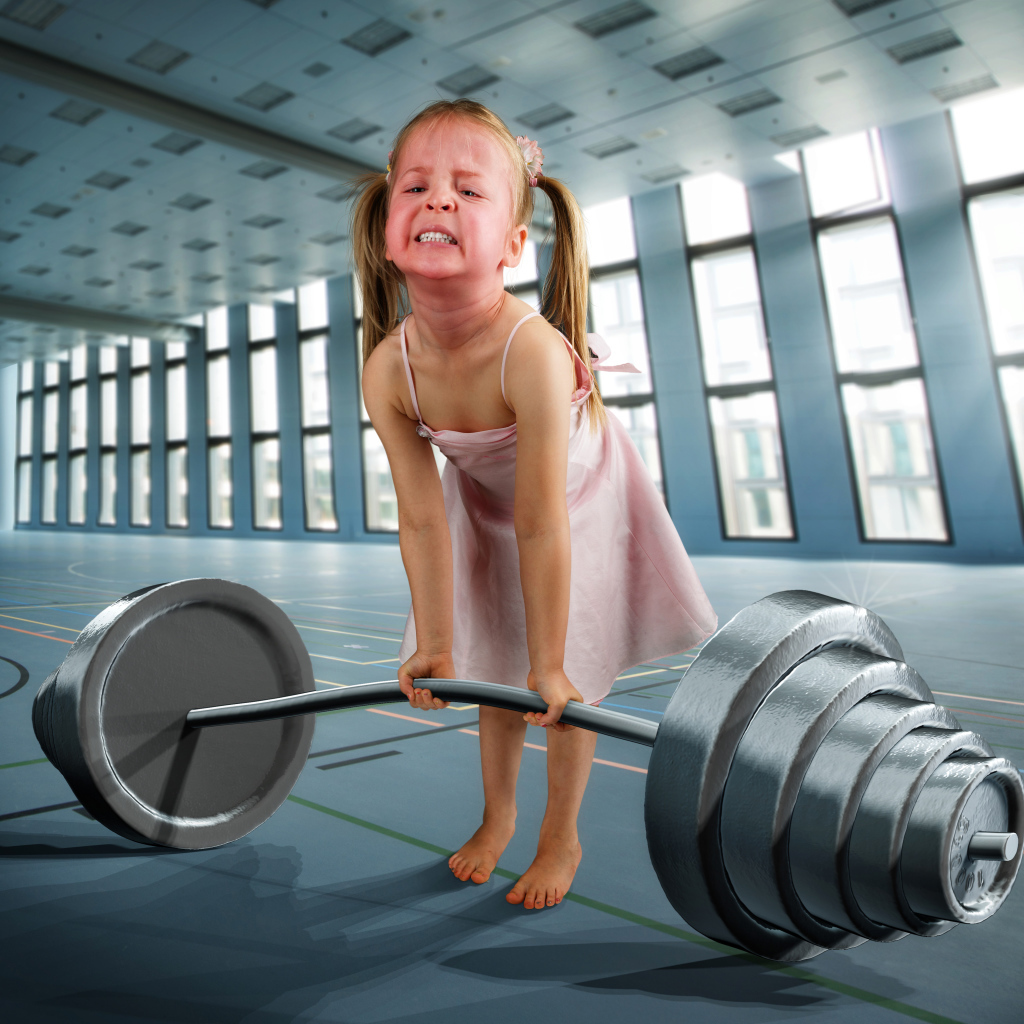 Смешная девочка пытается поднять тяжелую штангу