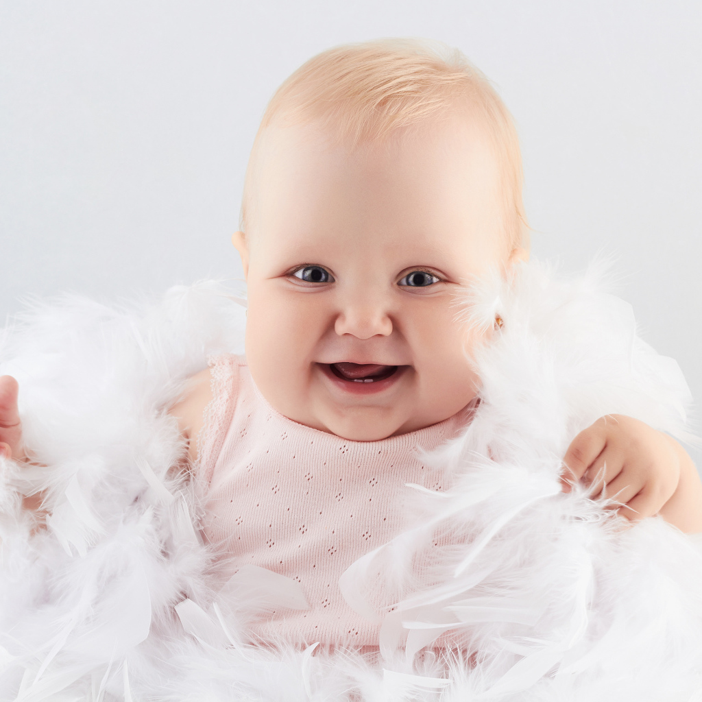 Забавная улыбающаяся маленькая девочка в белых перьях