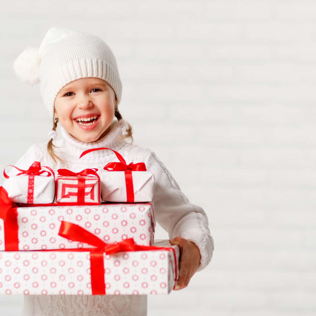 Смеющаяся девочка в белой шапке с новогодними подарками
