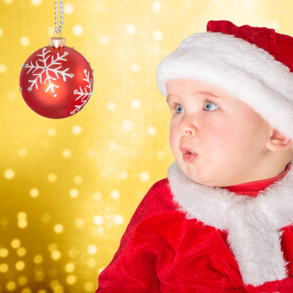 Маленький грудной ребенок в костюме Санты смотрит на елочный шар
