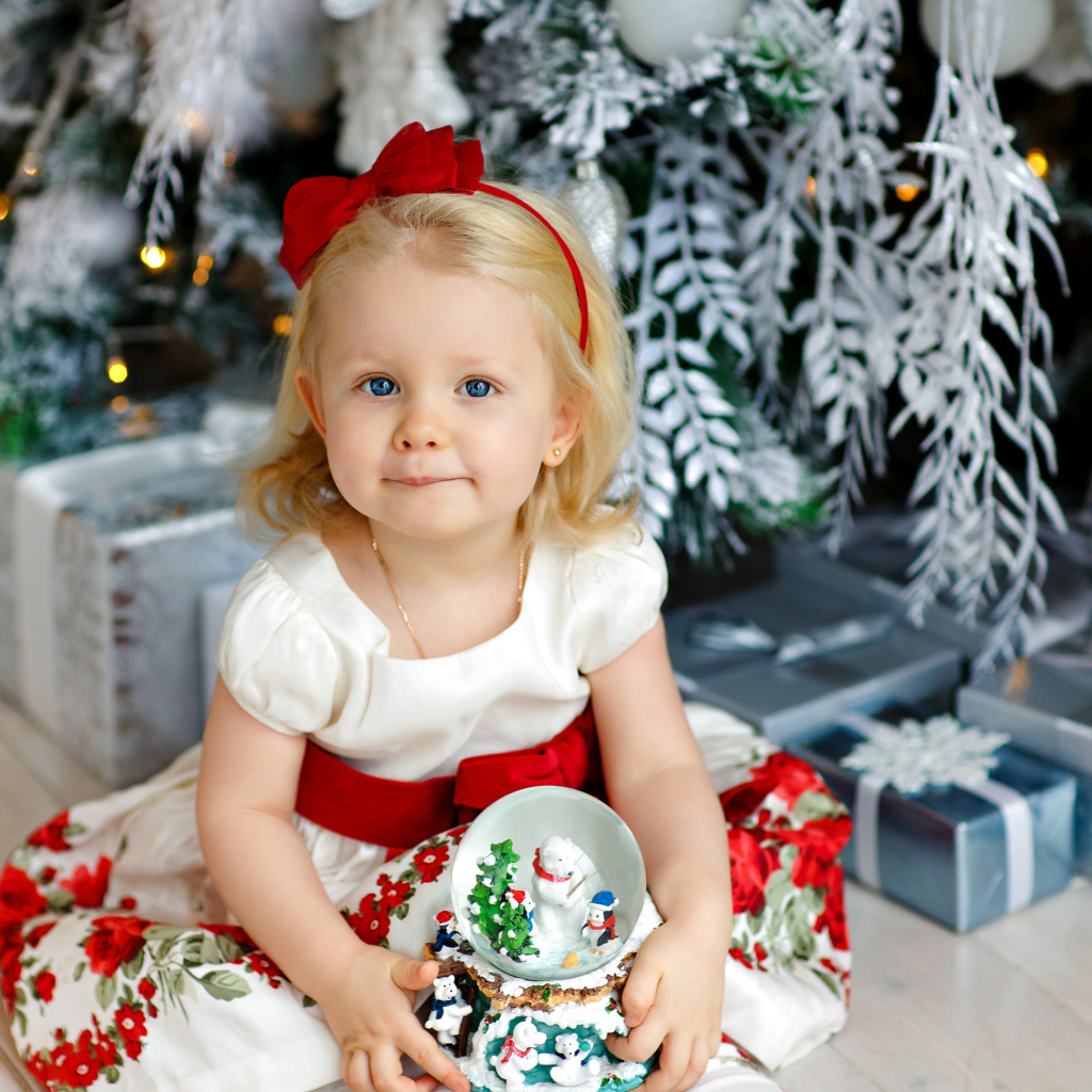 Маленькая девочка блондинка сидит с подарками под новогодней елкой