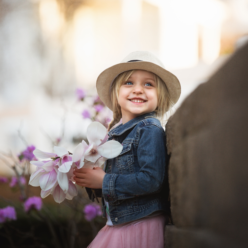 Маленькая голубоглазая улыбающаяся девочка в шляпе с букетом в руках