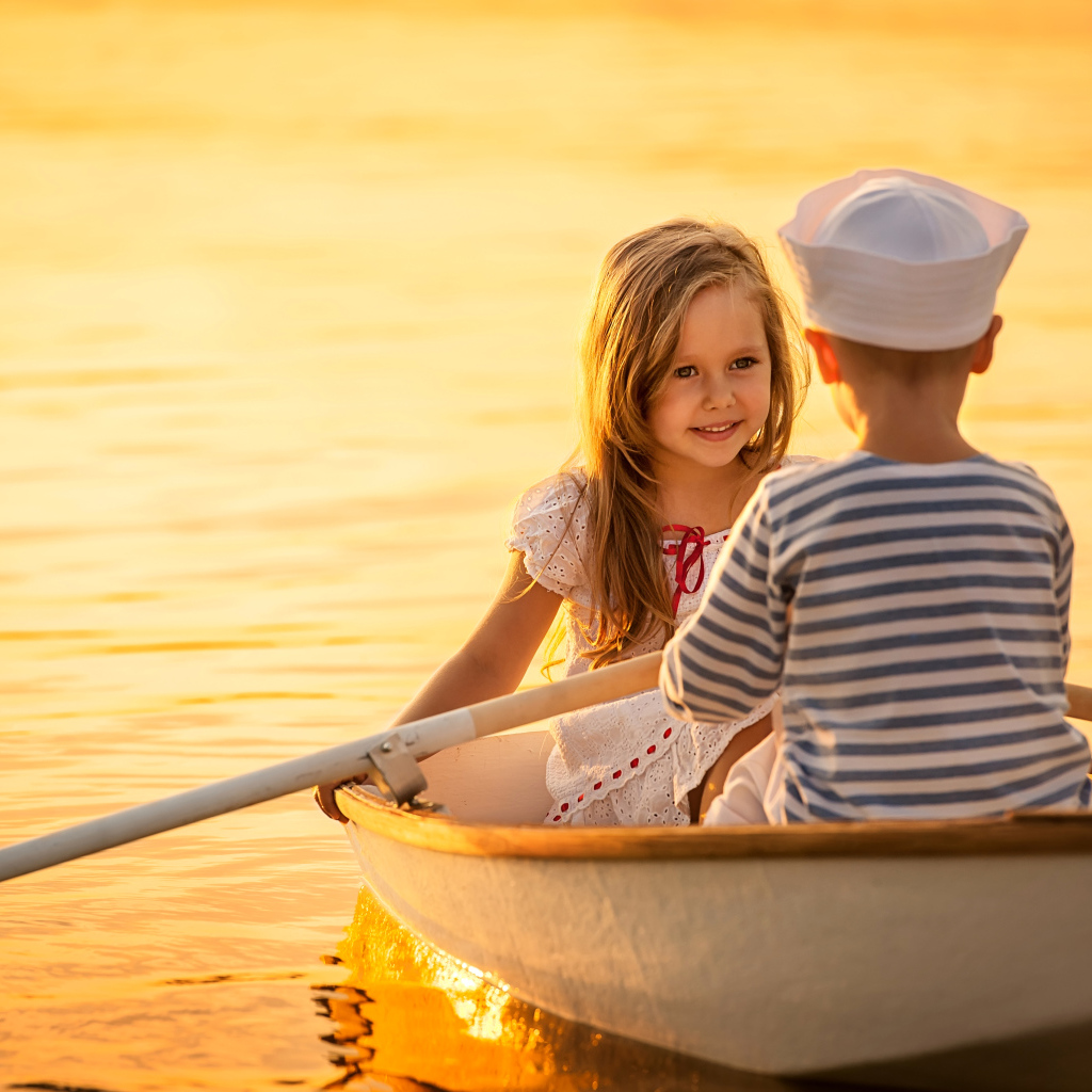 Маленькие мальчик и девочка плывут в лодке на закате солнца