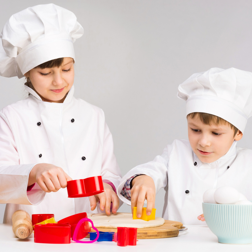 Маленькие мальчик и девочка готовят на кухне печенье