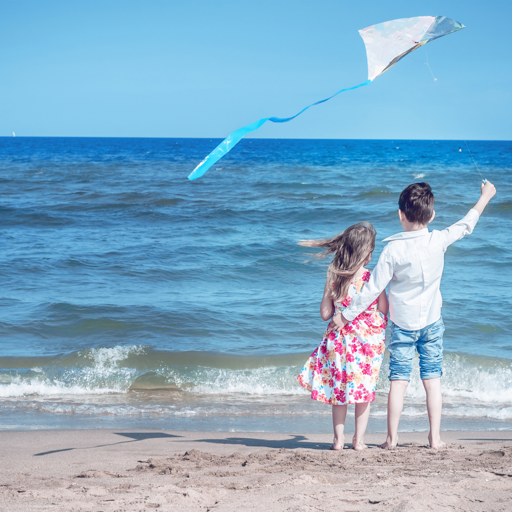 Маленькие мальчик и девочка запускаю воздушного змея на пляже