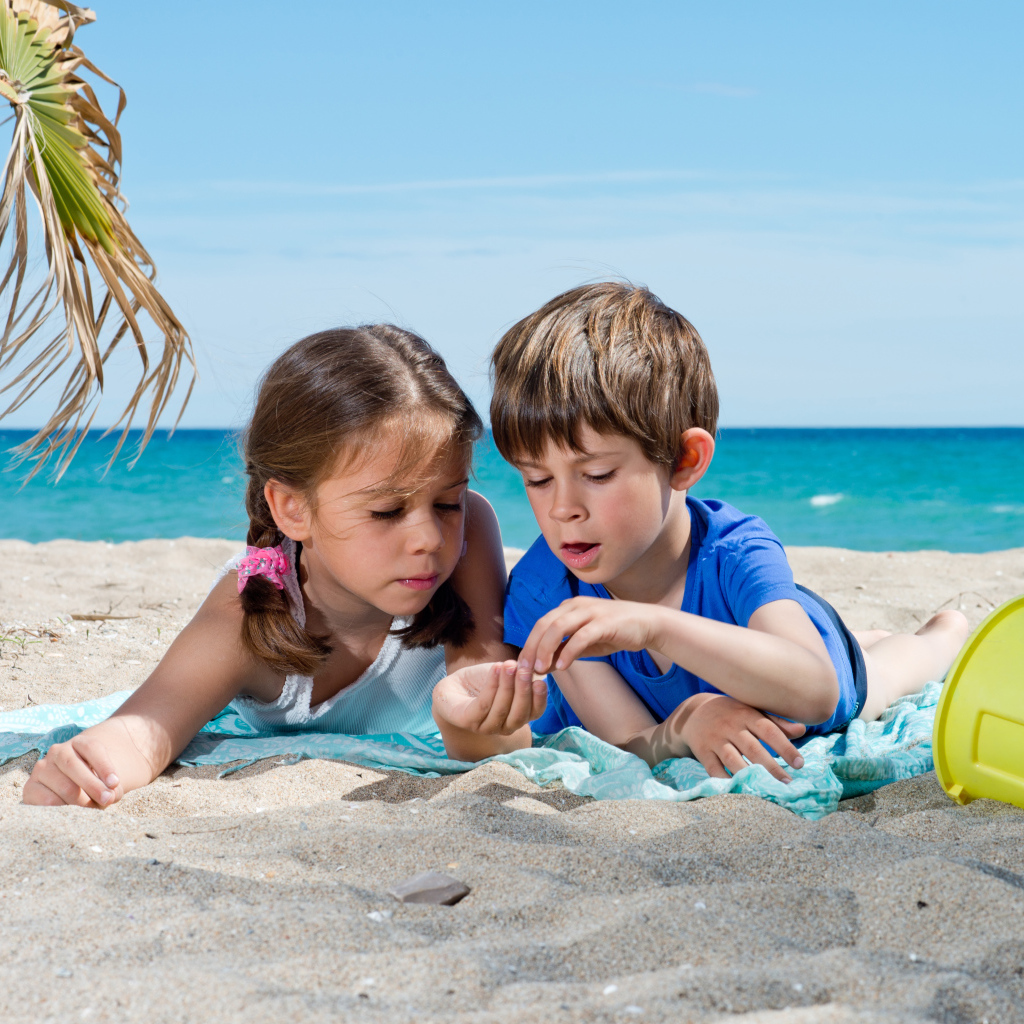 Маленькие мальчик и девочка играют на песке у моря