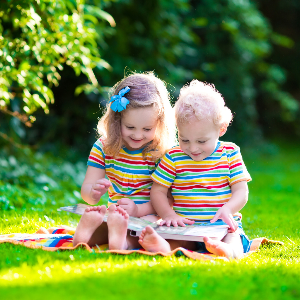 Маленькие мальчик и девочка читают книгу сидя на зеленой траве