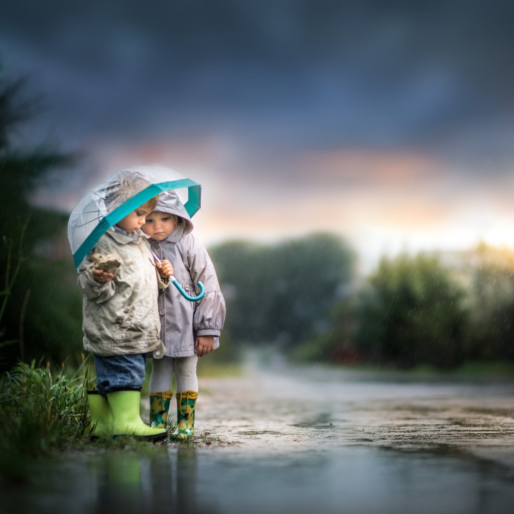 Маленькие мальчик и девочка под зонтом на дороге 