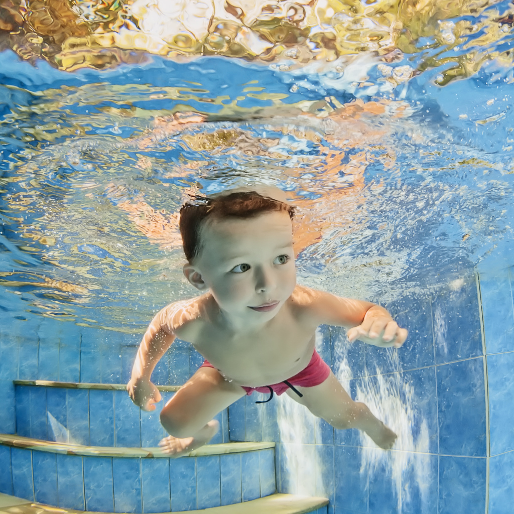Маленький мальчик плавает под водой в бассейне