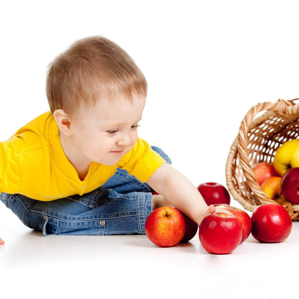 Маленький мальчик с корзиной спелых яблок на белом фоне