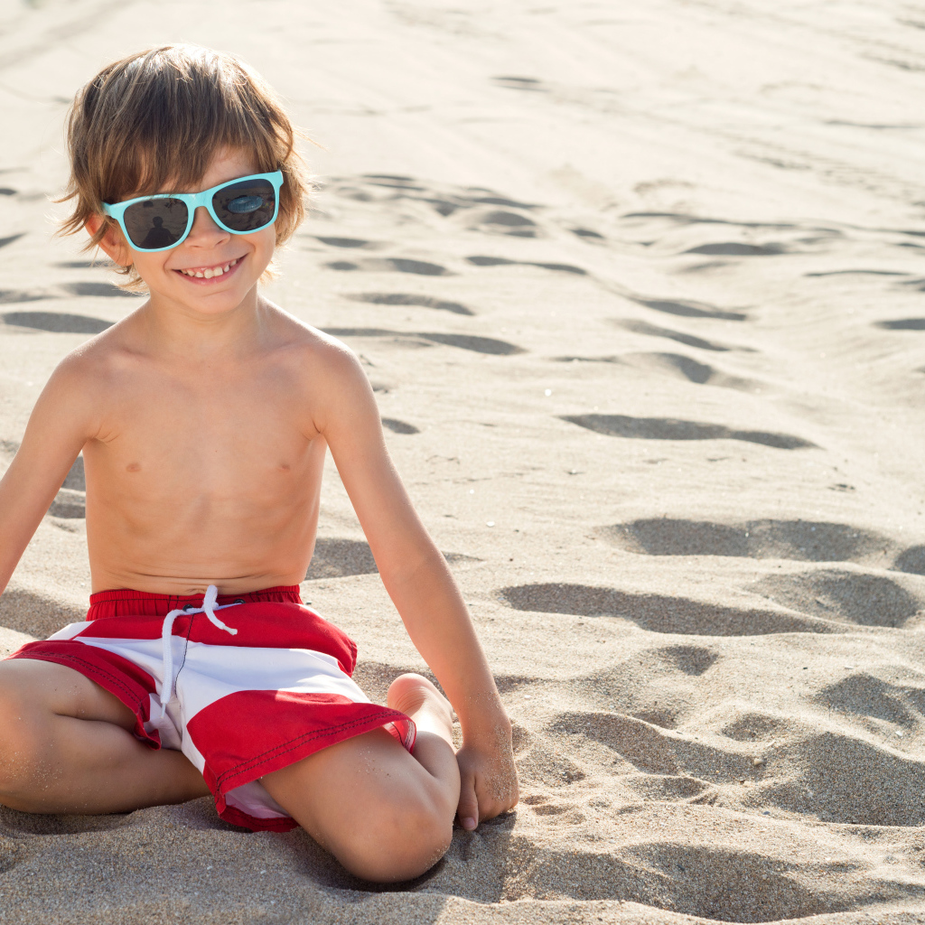 Маленький мальчик в очках сидит на песке на пляже