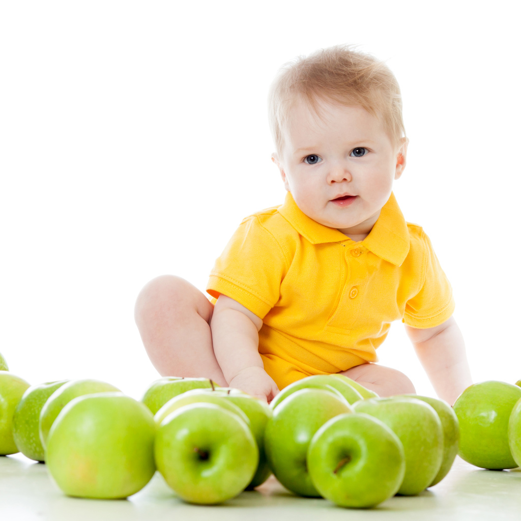 Маленький мальчик с зелеными яблоками на белом фоне