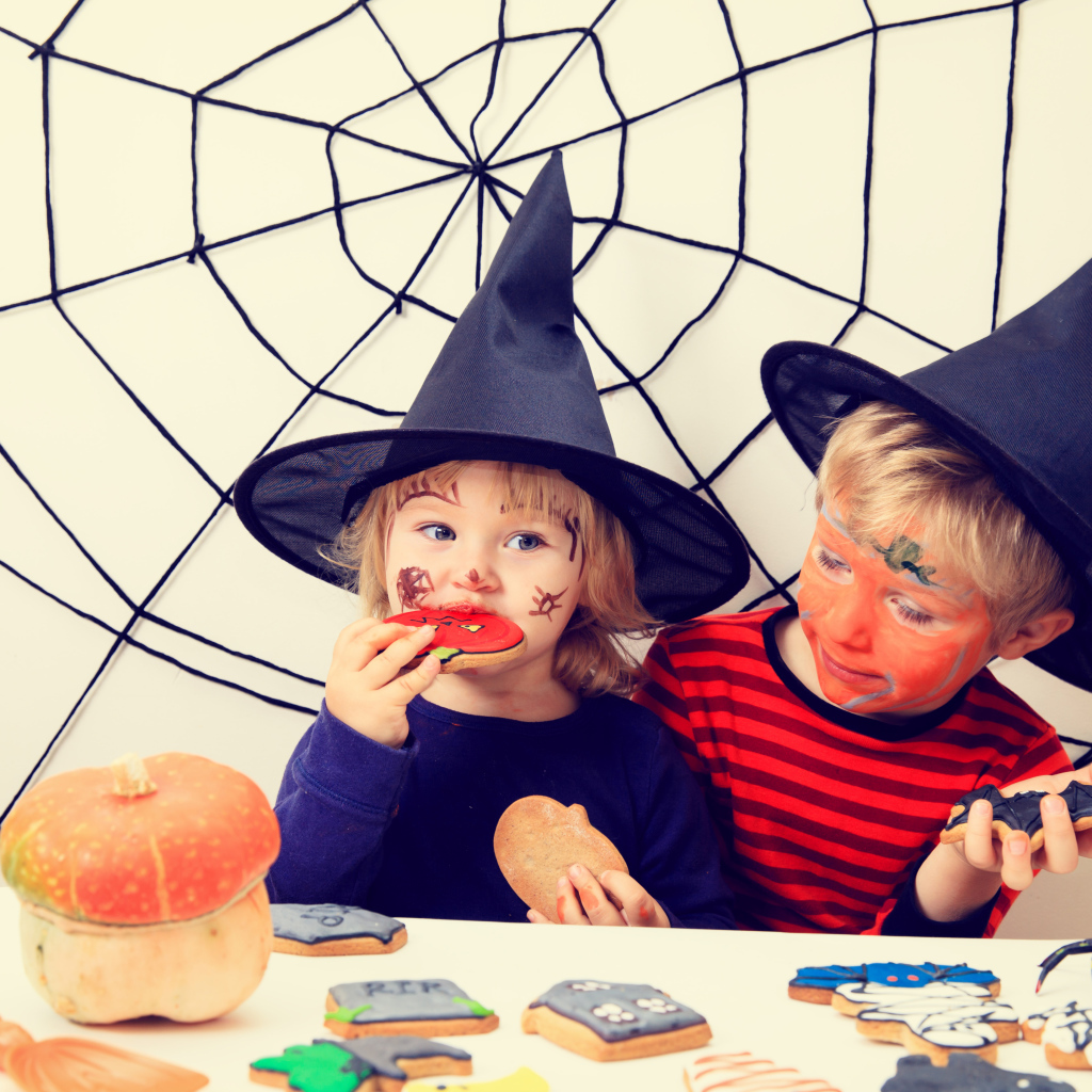 Маленькие дети в костюмах на Хэллоуин едят праздничные сладости