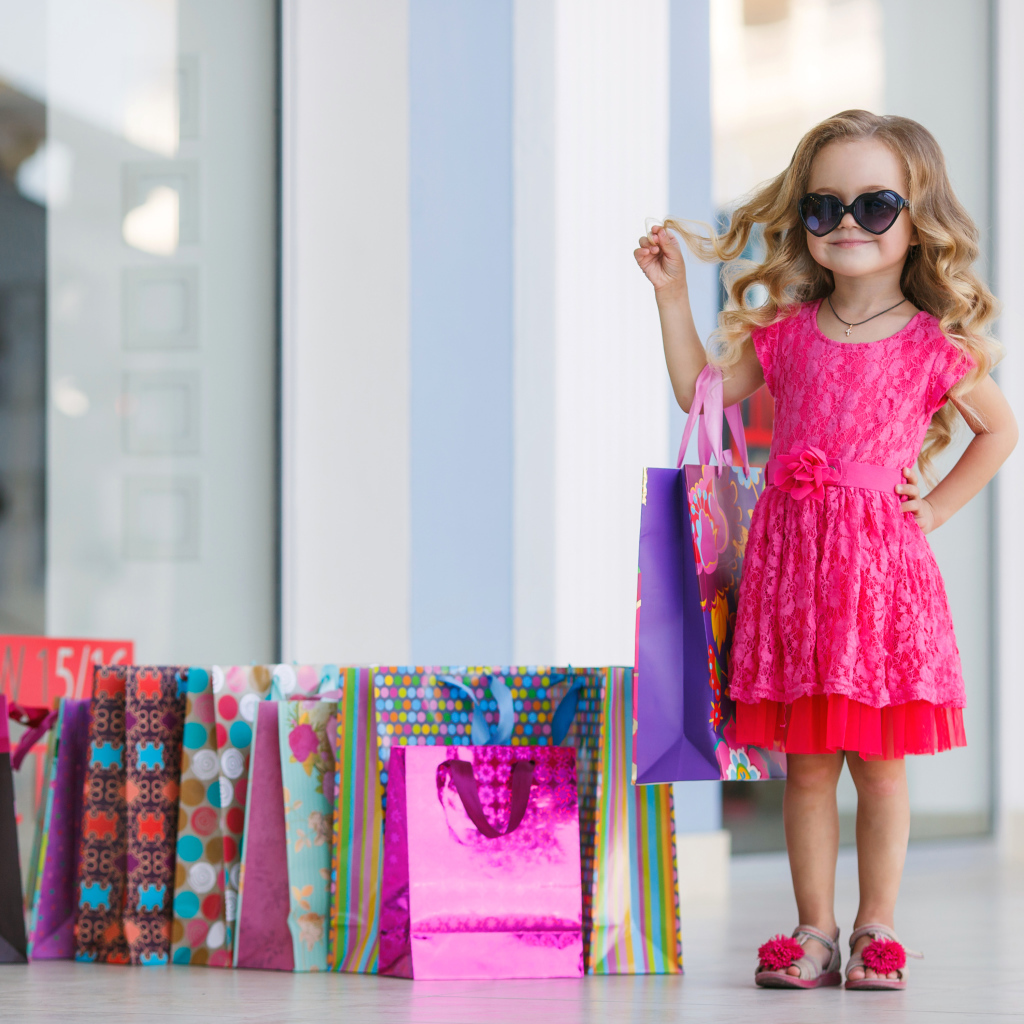 Маленькая модная девочка в красном платье с покупками