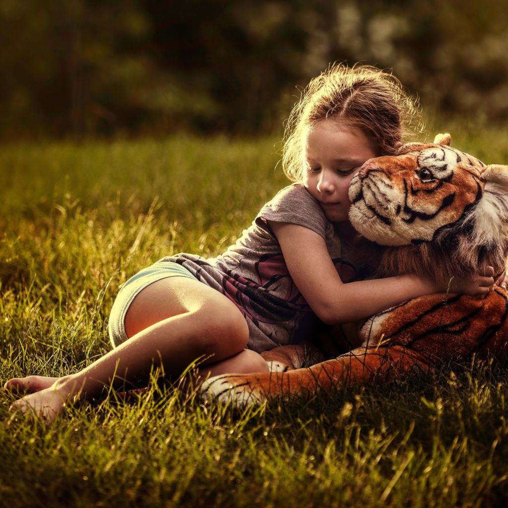 Маленькая девочка обнимает игрушечного тигра на зеленой траве