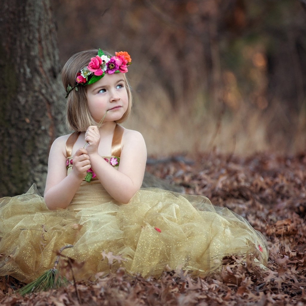 Маленькая девочка в красивом платье сидит на сухой листве