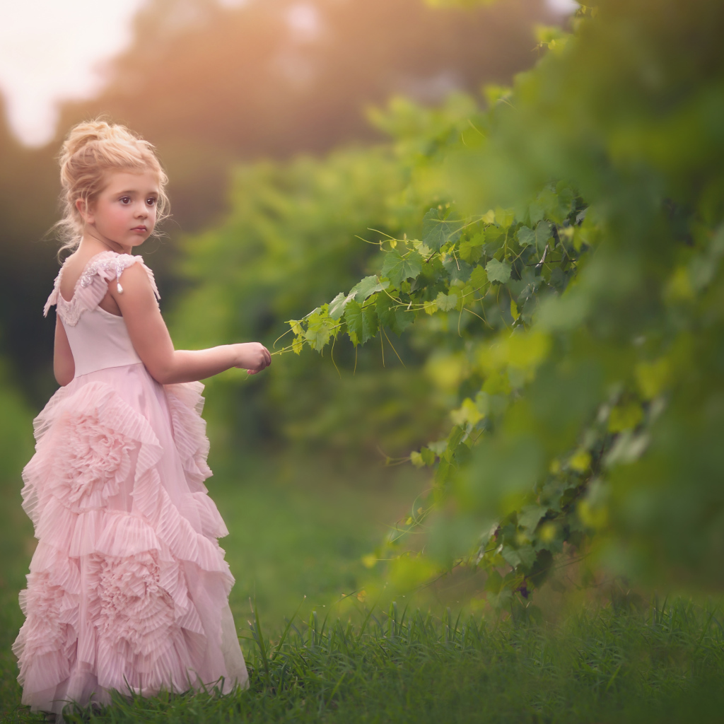Маленькая девочка в красивом розовом платье стоит на зеленой траве