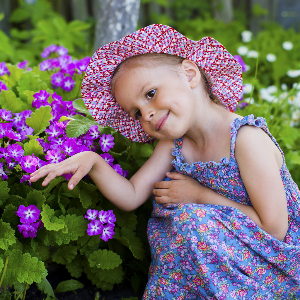 Маленькая девочка в шляпе рядом с фиолетовыми цветами