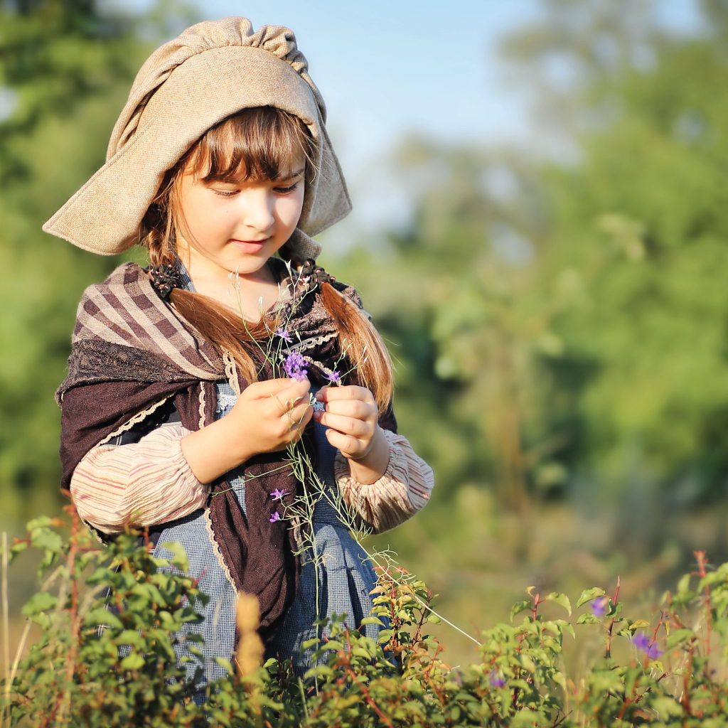 Маленькая девочка в костюме собирает травы